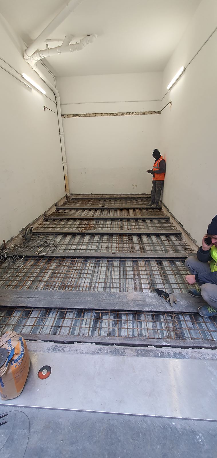Compagnons sur un plancher neuf en cours de ferraillage, entre les murs d'un immeuble existant