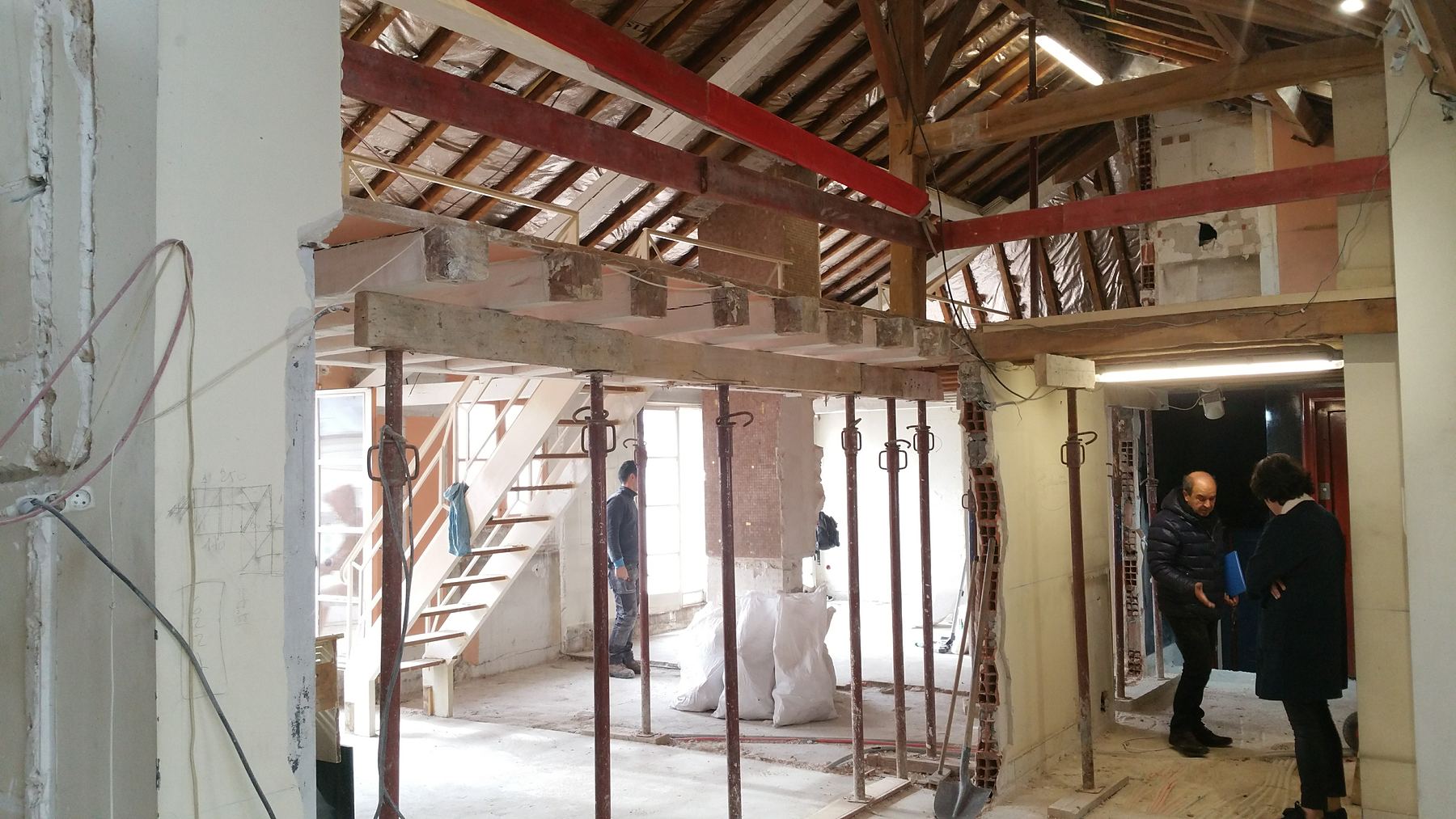 Visite d'un immeuble en cours de curage : charpente ancienne, poutres métalliques et étaiements sous les combles